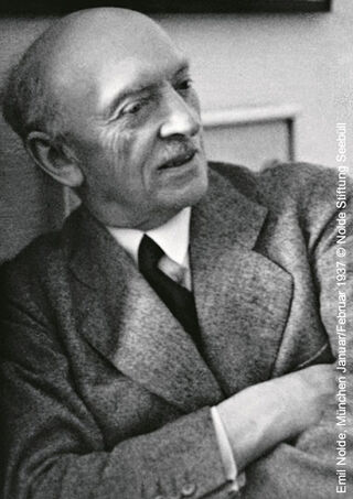 Photographie historique en noir et blanc du peintre expressionniste Emil Nolde, vêtu d'une veste en tweed, les bras croisés.