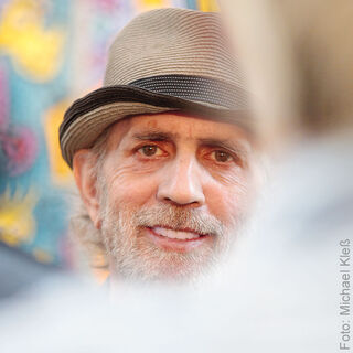 A close-up of the smiling Pop Art artist James Rizzi, with a grey beard and a hat.