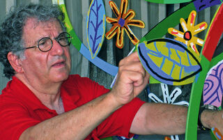 L'artiste et sculpteur contemporain israélien David Gerstein, portant des lunettes et un polo rouge, en train de travailler sur l'une de ses sculptures métalliques colorées aux motifs végétaux.