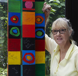 Die Künstlerin und Malerin Christine Kremkau steht mit Brille neben einer von ihr bunt bemalten, gemusterten Stele.