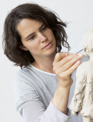 The sculptor Valerie Otte is working intently on a clay sculpture with her tools.